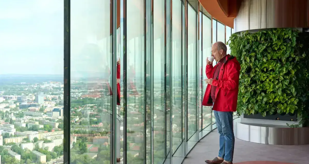 Mężczyzna pije kawę, podziwiając panoramę Wrocławia z tarasu widokowego. Sprawdź Sky Tower Wrocław cennik, by poznać ceny biletów.
