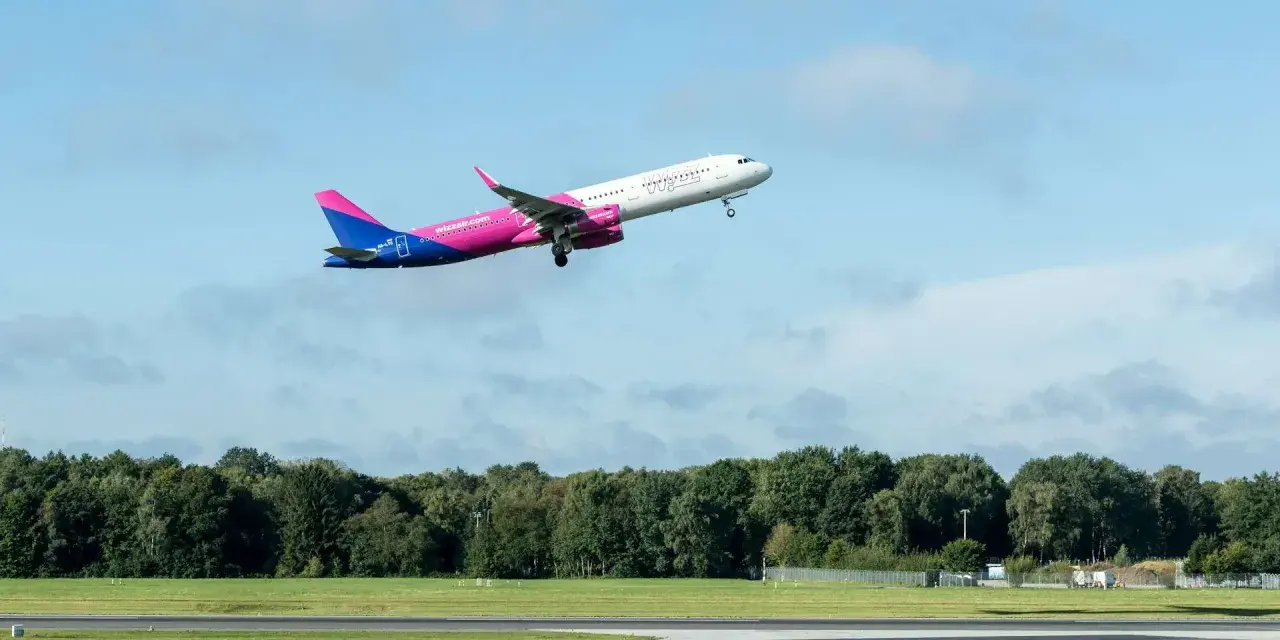 Samolot Wizz Air wznosi się na tle błękitnego nieba z chmurami.