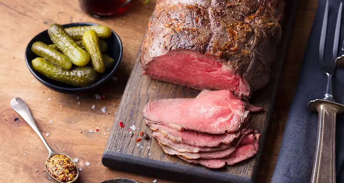 Un délicieux roti de boeuf, tranché et servi avec des cornichons, de la moutarde et une boisson foncée.