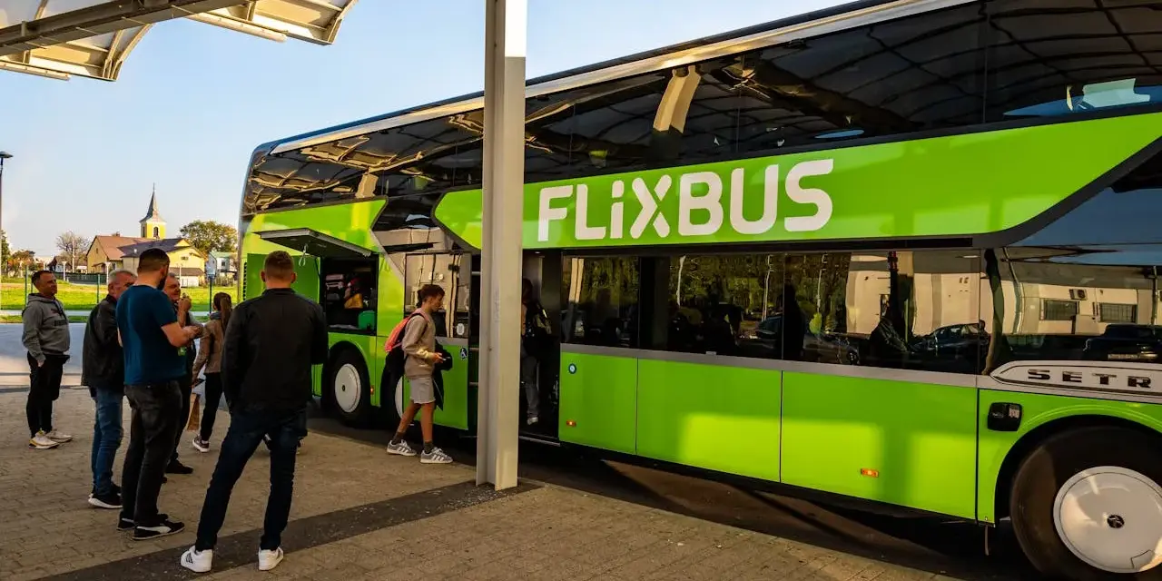 Zielony autobus FlixBus na przystanku, z pasażerami wsiadającymi i wysiadającymi.