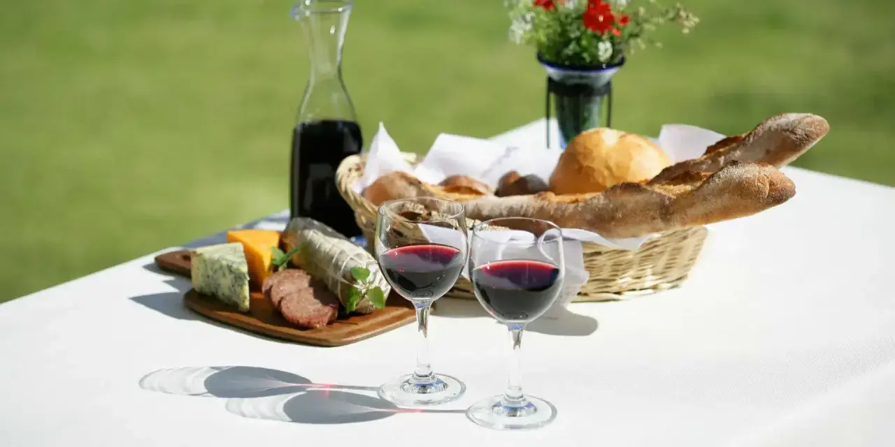 Dwa kieliszki pełne rubinowego pinot noir wina, obok deska serów, wędlin i kosz świeżego pieczywa.