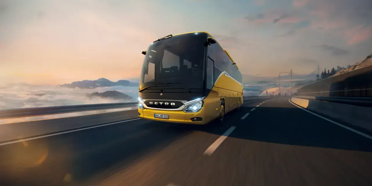 Żółty setra autobus pędzi po autostradzie wśród chmur i gór, w stronę mostu.