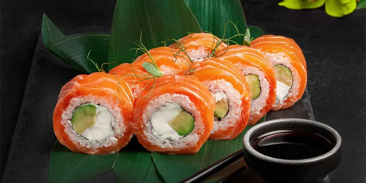 Roladki sushi z łososiem i awokado, podane na liściach. Inspiracja, jak zrobić sushi.