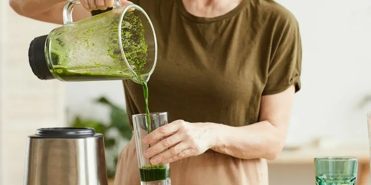 Kobieta nalewa zielony koktajl położnej do szklanki. Na blacie widać blender, awokado i jabłko.