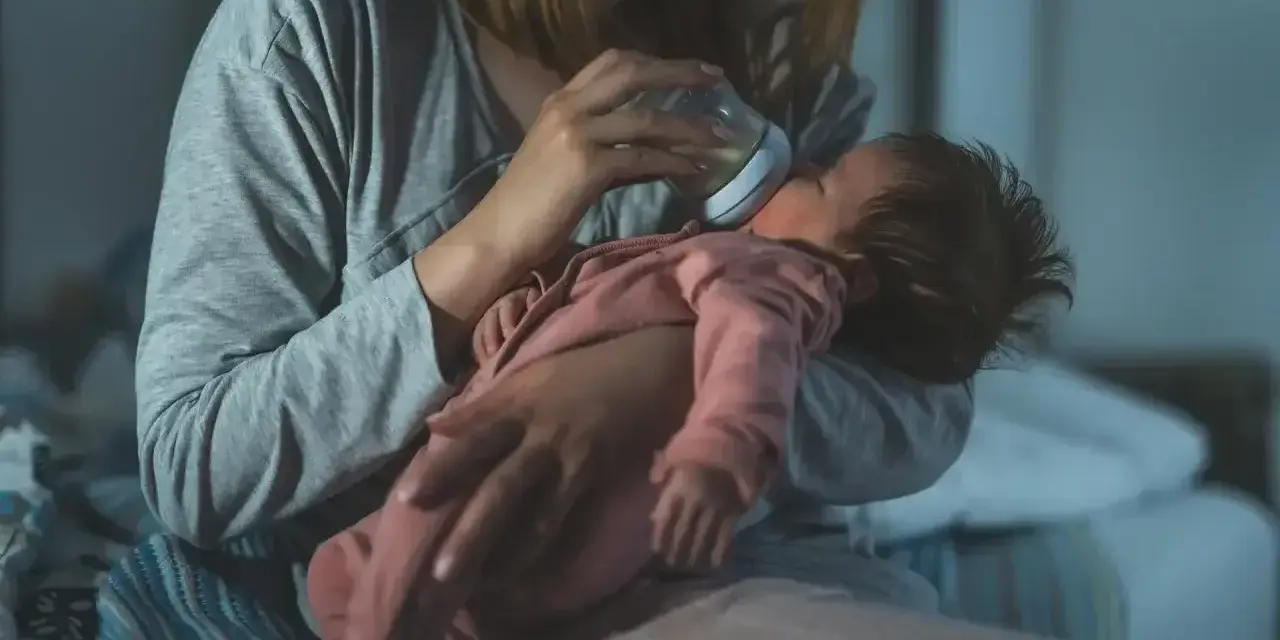 Mama karmi butelką niemowlę, które obudziło się w nocy z płaczem.
