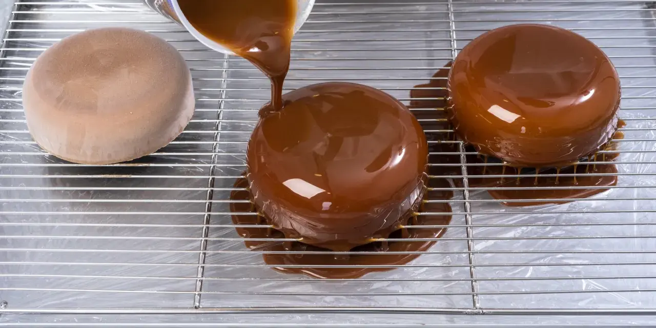 Dolce lucido ricoperto da una colata di cioccolato. La glassa scende sui lati, creando un effetto invitante.