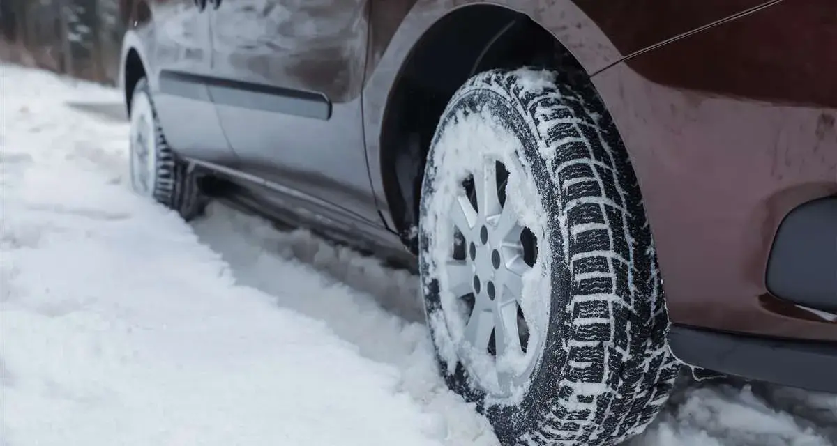 Un'auto marrone avanza su una strada innevata, le ruote dotate di pneumatici chiodati per affrontare il ghiaccio e la neve.