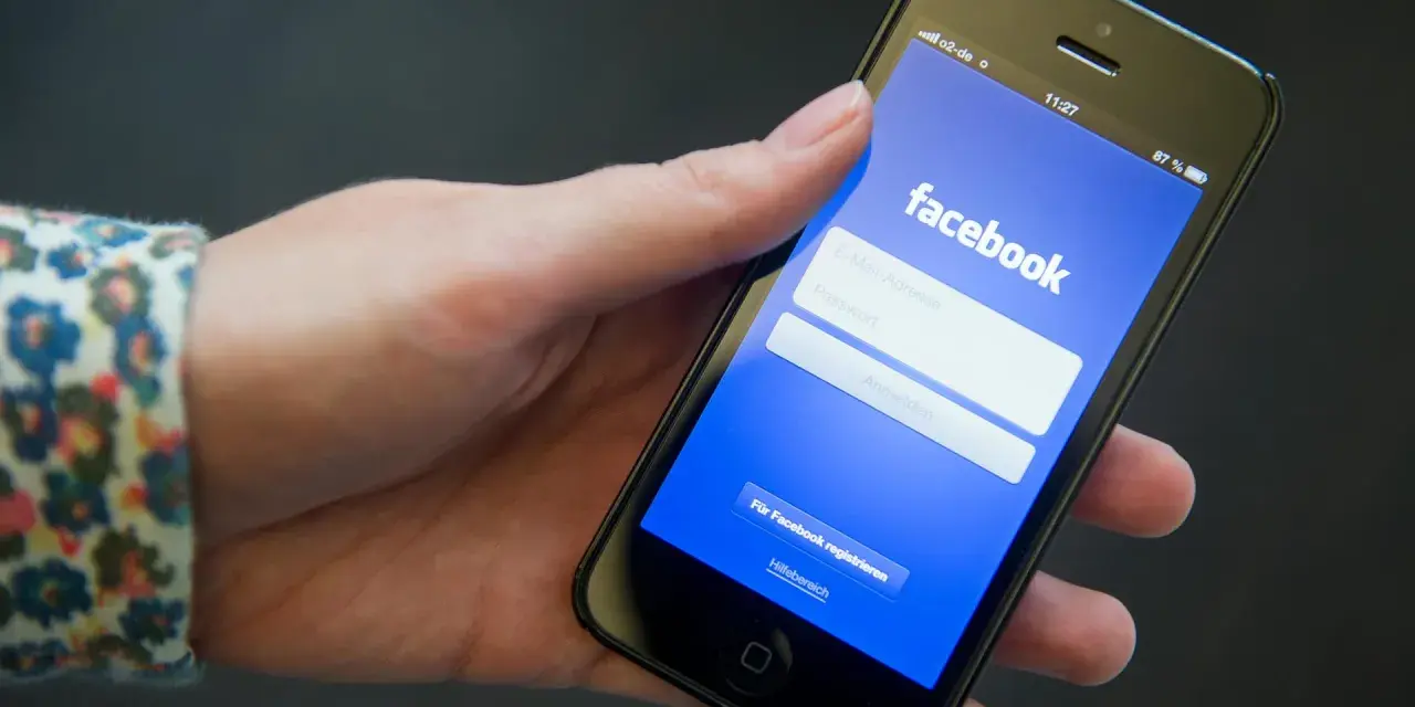 Eine Hand hält ein Smartphone mit der Facebook-Anmeldeseite.