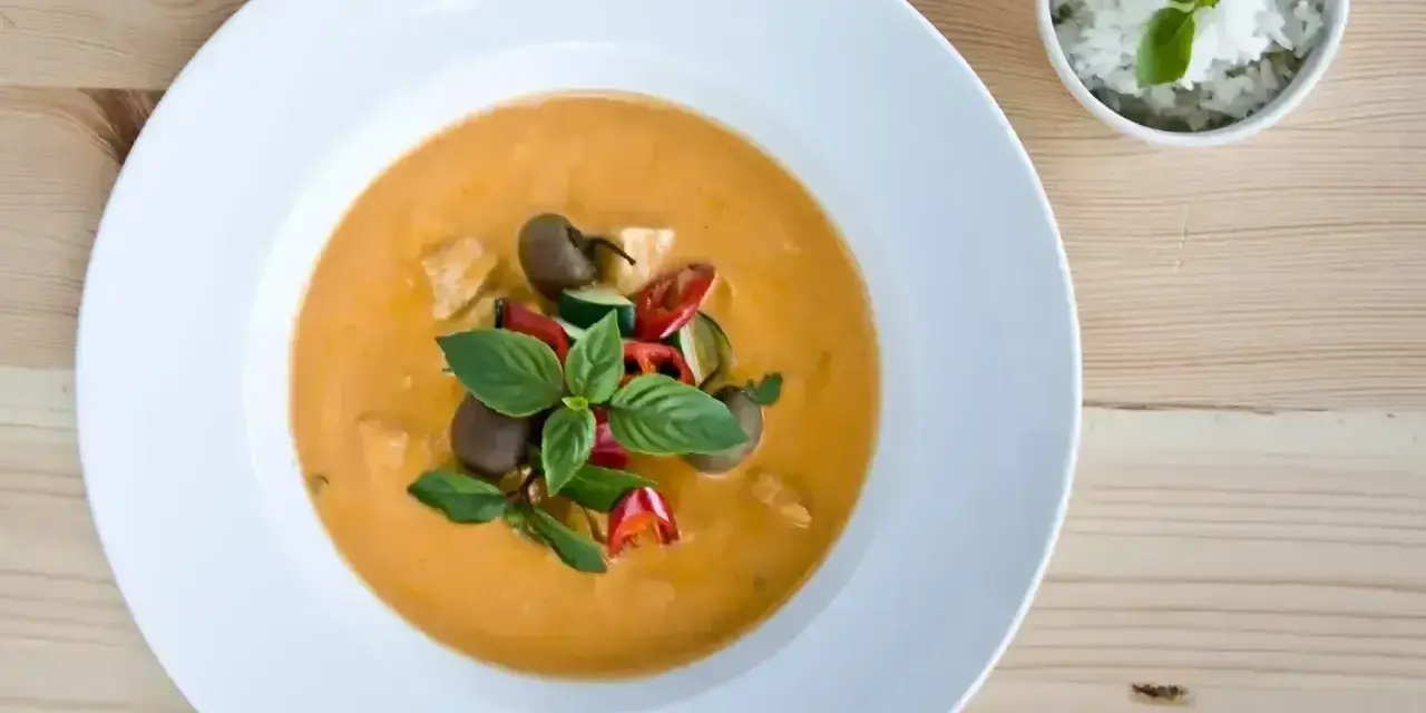 Aksamitny, pomarańczowy **thai red curry** z kawałkami kurczaka, cukinii, pomidorków i bazylii, podany z ryżem.