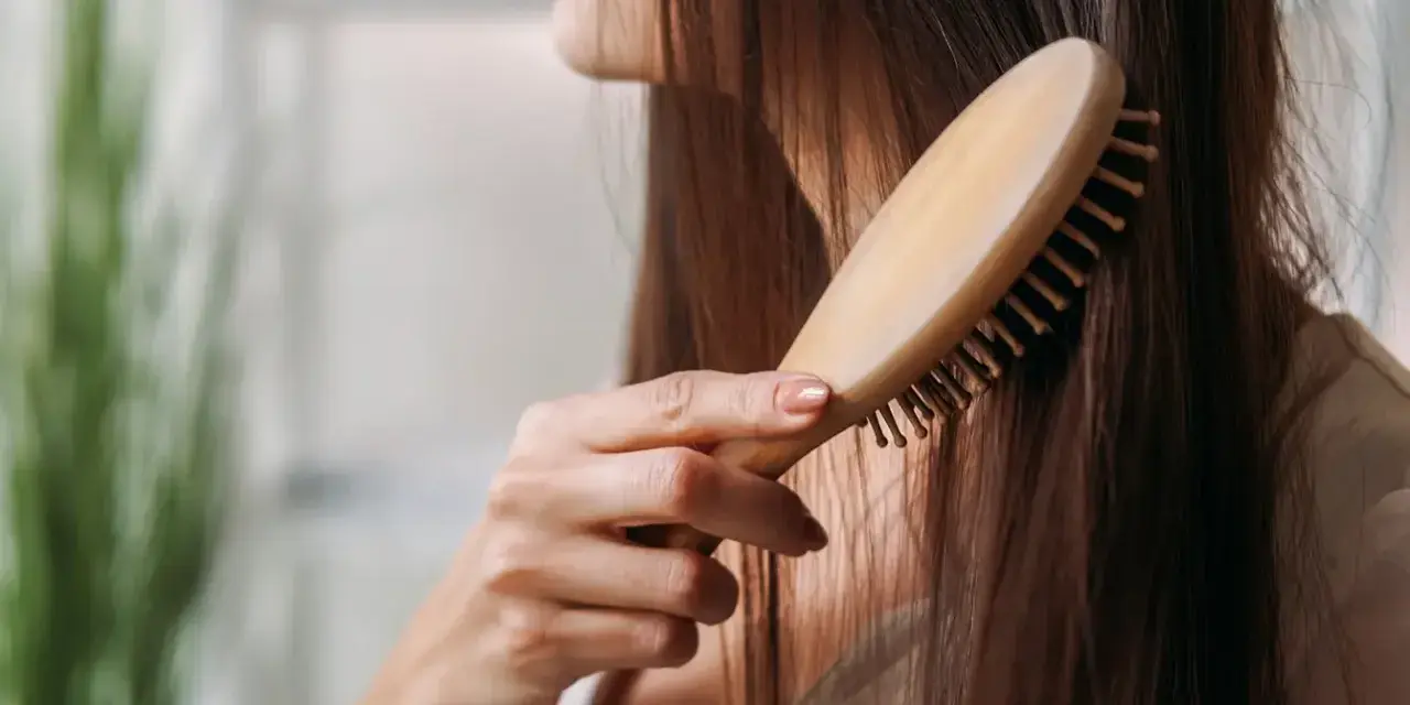 Eine Frau kämmt ihr langes, dunkles Haar mit einer Holzbürste. Sie achtet auf ihre Haare, um Haarausfall bei Frauen im Alter vorzubeugen.