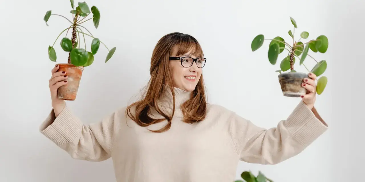 Mujer sonriente con gafas sostiene dos plantas altas de interior.