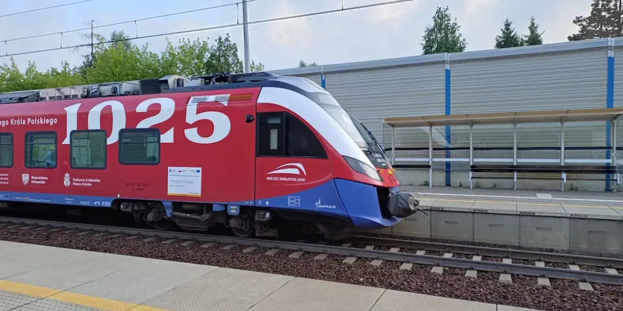 Czerwony pociąg Kolei Małopolskich z numerem 1025 na bocznym panelu, gotowy do podróży z Kielc do Krakowa, stoi na peronie.