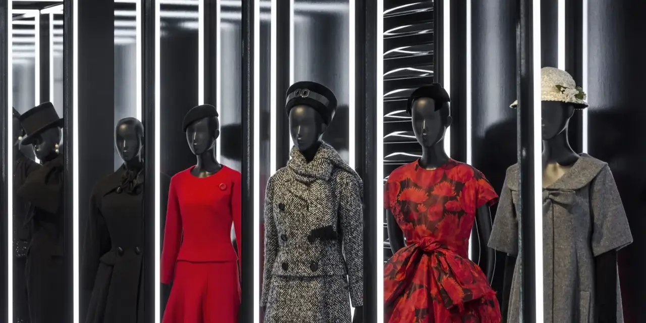 Manichini con abiti eleganti, un omaggio all'eleganza e all'origine Dior. Rossi, neri e grigi, con cappelli e sciarpe.