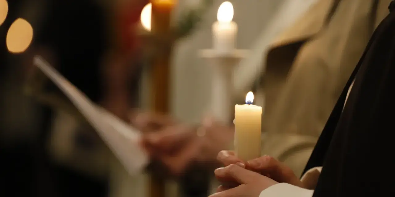 Dłonie trzymają płonące świece, symbolizujące poświęcenie ognia podczas uroczystości.