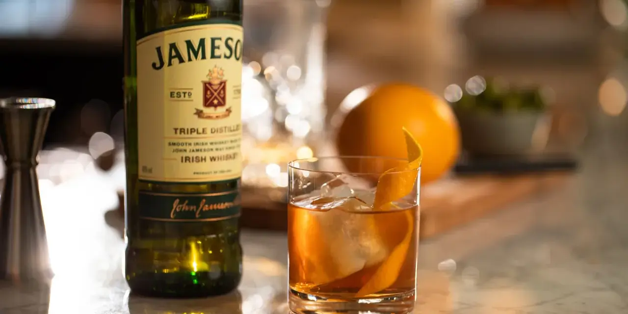 Old Fashioned na bourbonie czy na żytniej whisky? Jameson Irish Whiskey obok drinka z pomarańczą i lodem.