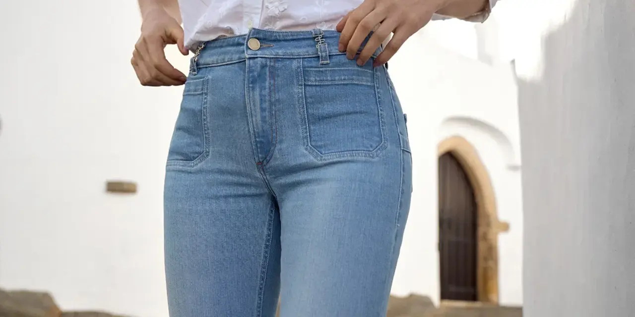 Mujer con vaqueros de tiro alto y camisa blanca, ajustándose la cintura.