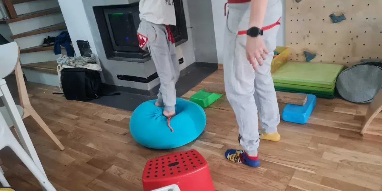 Dziecko ćwiczy równowagę na niebieskiej poduszce, część domowej ścieżki sensorycznej dla dzieci.