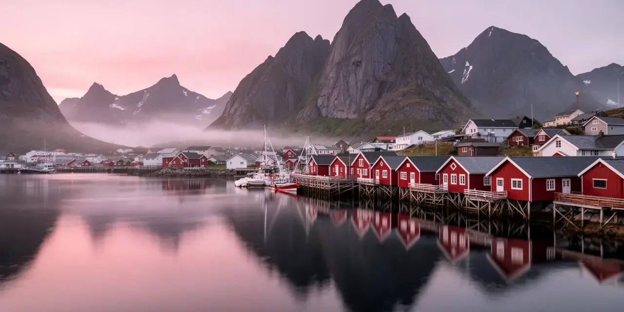 Röda fiskestugor vid vattnet i Lofoten, med berg och rosa himmel. En dröm om norrsken.