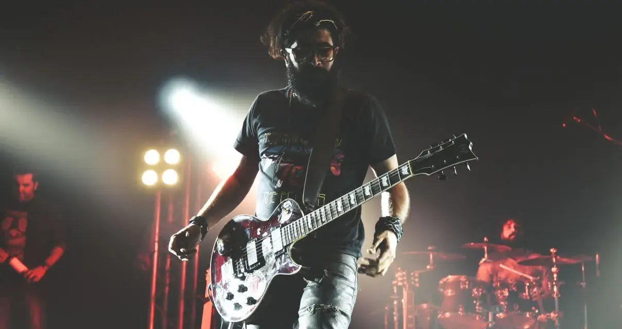 Un guitariste charismatique d'un groupe de rock mythique, en pleine performance sur scène, éclairé par des projecteurs.