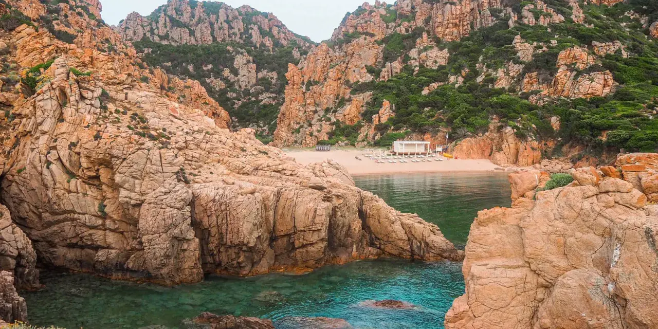 Skaliste wybrzeże Sardynii z turkusową wodą i piaszczystą plażą. Idealne miejsce, by odkryć, co zobaczyć na Sardynii.