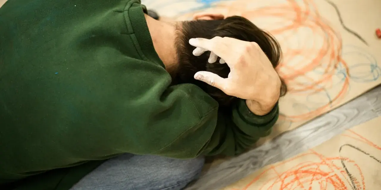 Kind mit weißer Farbe an den Fingern, das sich auf einem Boden mit Kritzeleien befindet. Möglicherweise ein Test zur affektiven Dysregulation.