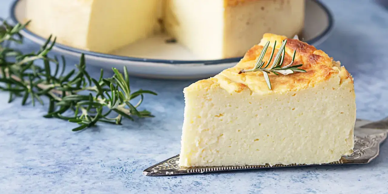 Una fetta di torta di ricotta soffice e dorata, guarnita con rosmarino, su un piatto da torta.