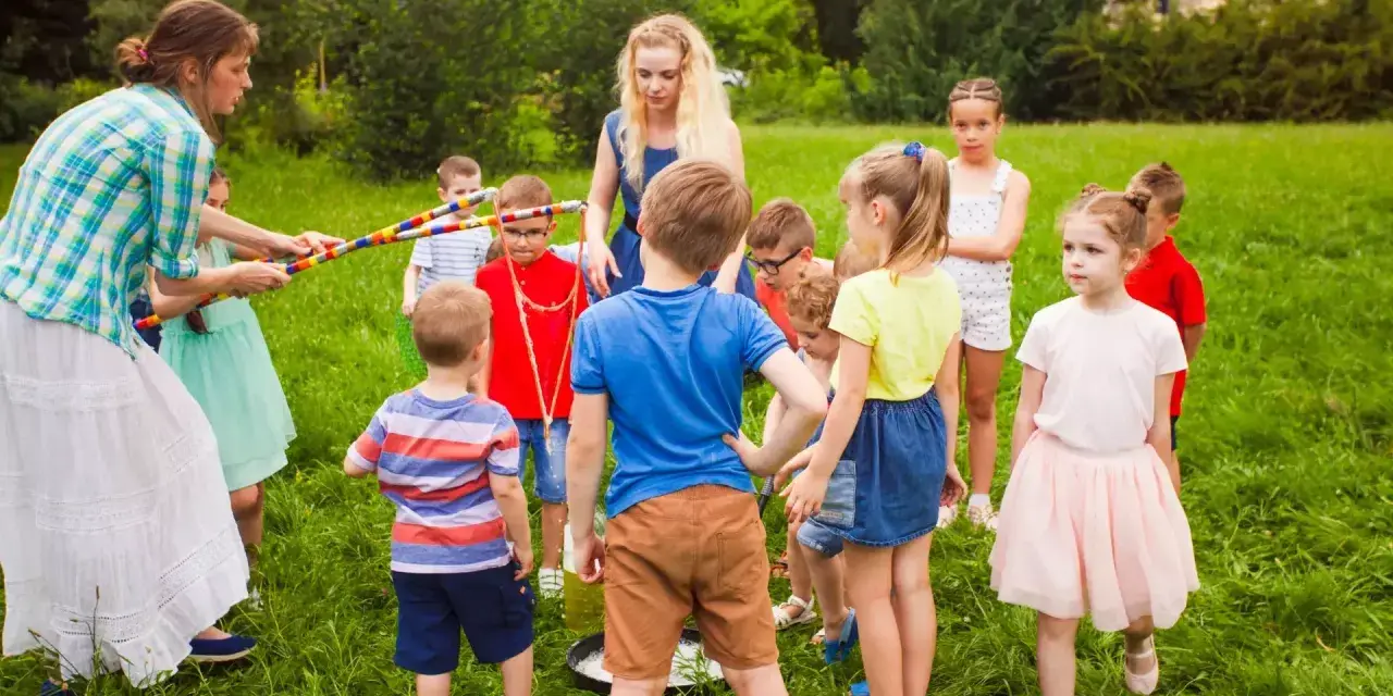 Des animateurs et des enfants jouent dehors dans l'herbe avec des cerceaux colorés.