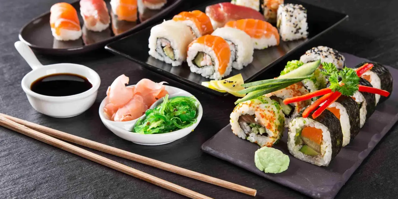 Pyszne sushi, w tym uramaki, z łososiem i awokado, podane z imbirem, wasabi i sosem sojowym.