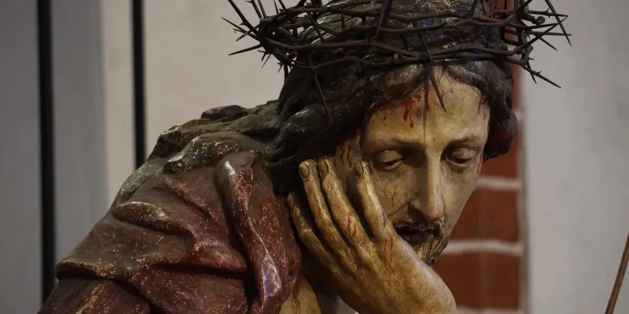 Chrystus Frasobliwy, rzeźba z koroną cierniową i krwawymi ranami, zamyślony, opiera głowę na dłoni.