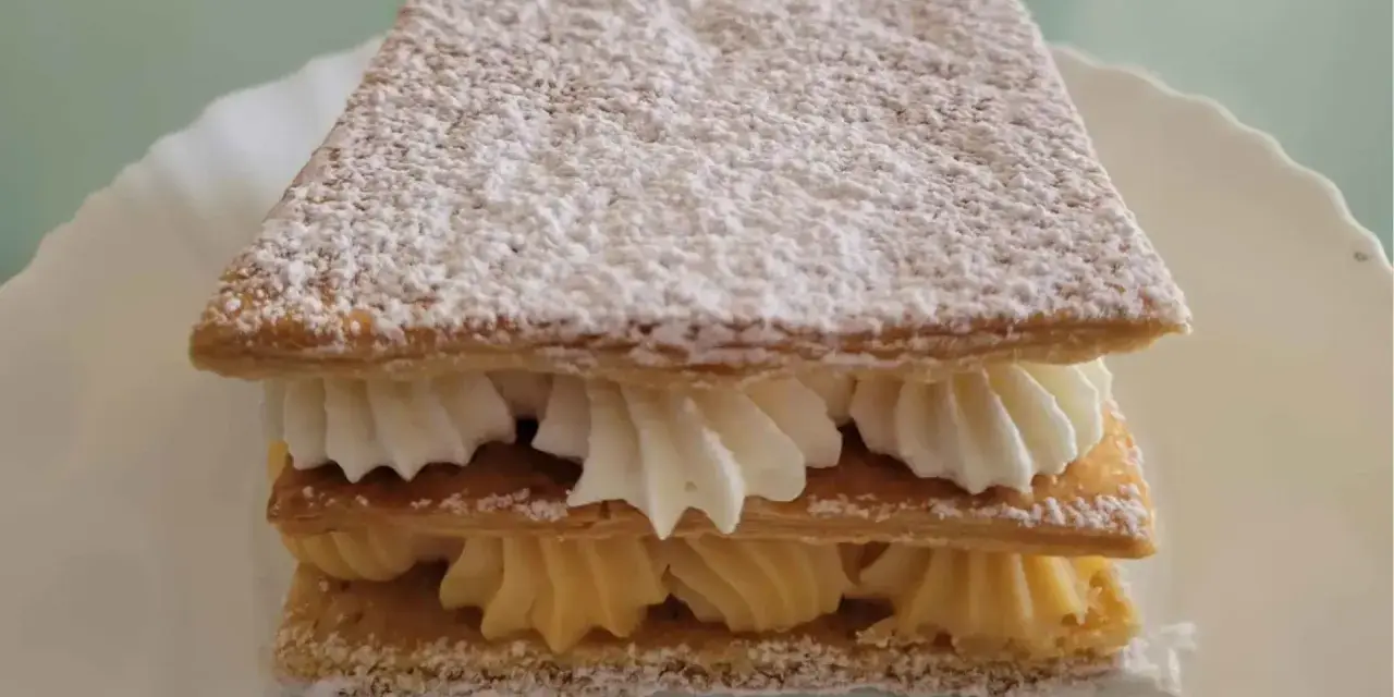 Delicioso milhojas de crema, con capas crujientes de hojaldre y rellenos de crema pastelera y nata montada, espolvoreado con azúcar glas.