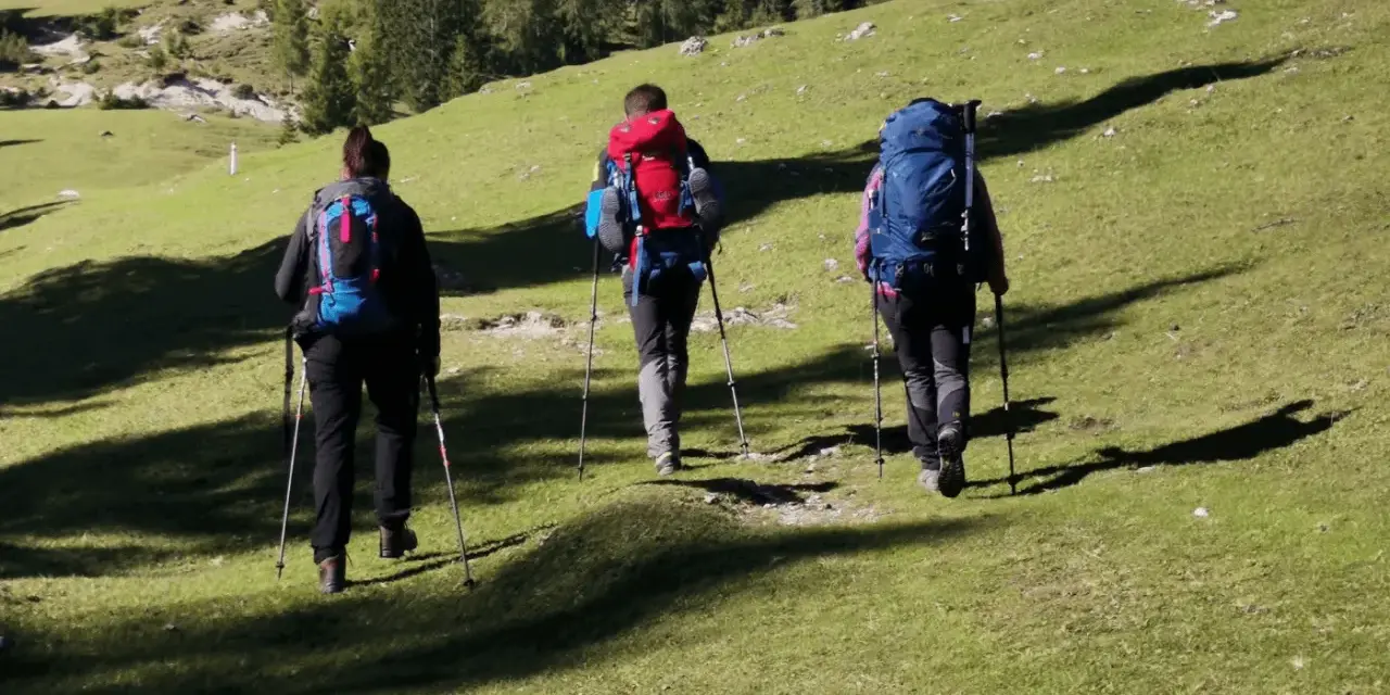 Tre escursionisti con zaini e bastoncini affrontano un sentiero in salita, godendosi i **percorsi trekking toscana**.