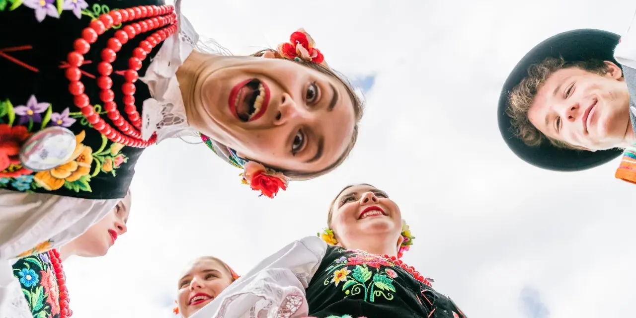 Uśmiechnięci młodzi ludzie w barwnych strojach ludowych, żywa ludowa twórczość artystyczna.