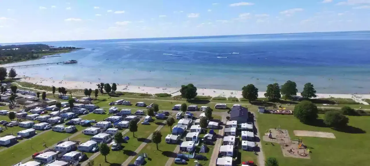 En stor campingplats vid havet nära Kalmar. Husvagnar och husbilar står uppradade på gräsmattor, med en strand och brygga i bakgrunden.
