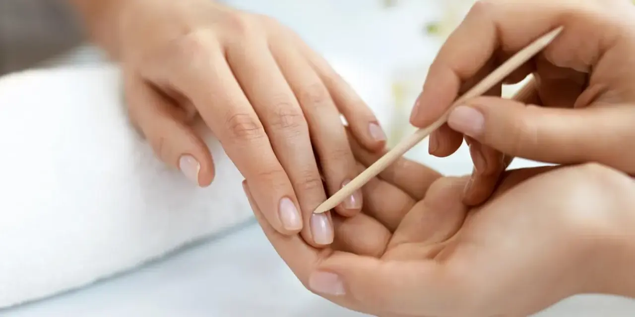 Delikatne dłonie poddawane zabiegowi manicure biologiczny. Skórki są starannie odsuwane patyczkiem, przygotowując paznokcie do dalszej pielęgnacji.