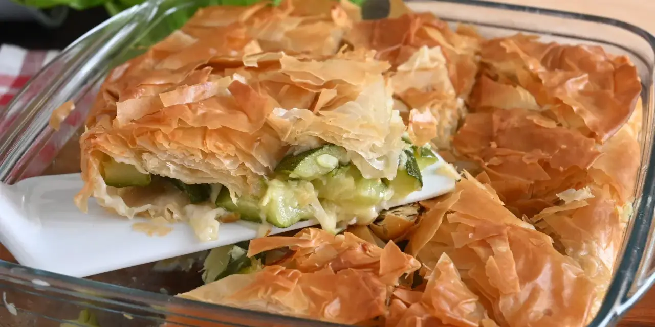 Una fetta di torta salata con zucchine, con croccante pasta sfoglia dorata e ripieno filante.