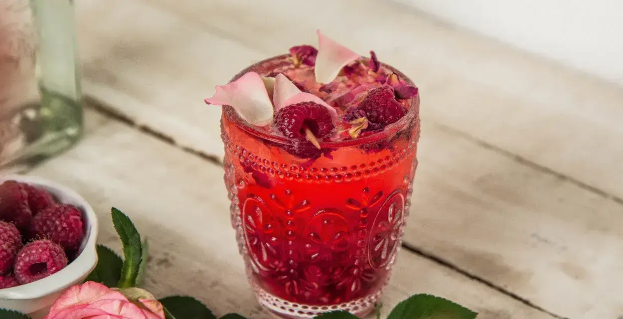 Orzeźwiający drink z malinami, ozdobiony płatkami róż i świeżymi malinami. Idealny na letnie popołudnie.