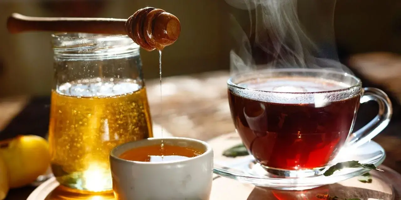 Une cuillère en bois verse du miel doré dans une tasse de thé fumante. Un délice réconfortant de miel dans eau chaude.