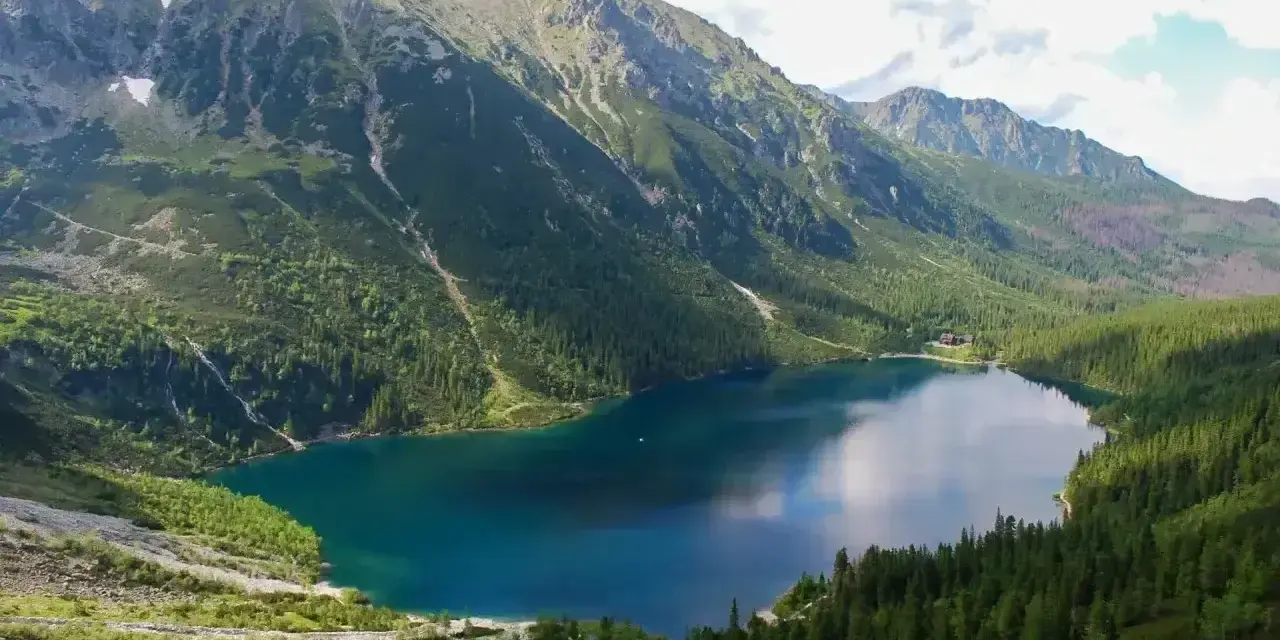 Górskie jezioro Morskie Oko otoczone zielonymi lasami i skalistymi szczytami.