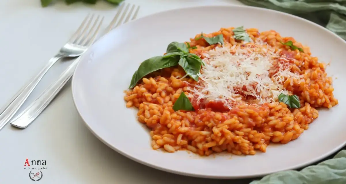 Un cremoso risotto al pomodoro, guarnito con basilico fresco e parmigiano grattugiato, pronto per essere gustato.