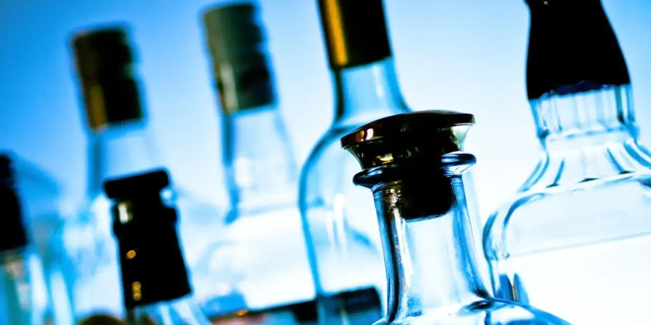 Kilka szklanych butelek alkoholu na niebieskim tle.