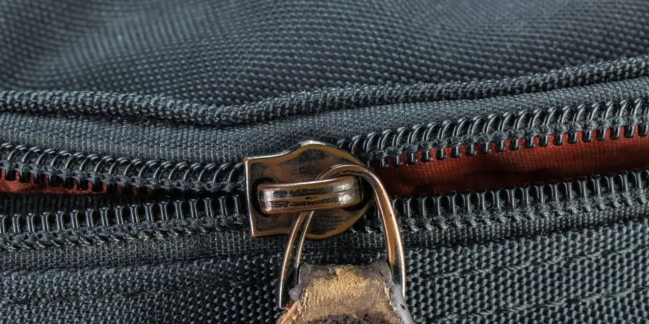 Nahaufnahme eines Reißverschlusses an einer schwarzen Tasche. Der Schieber ist aus Metall und leicht abgenutzt, was auf die Notwendigkeit hinweist, den Reißverschluss zu reparieren.