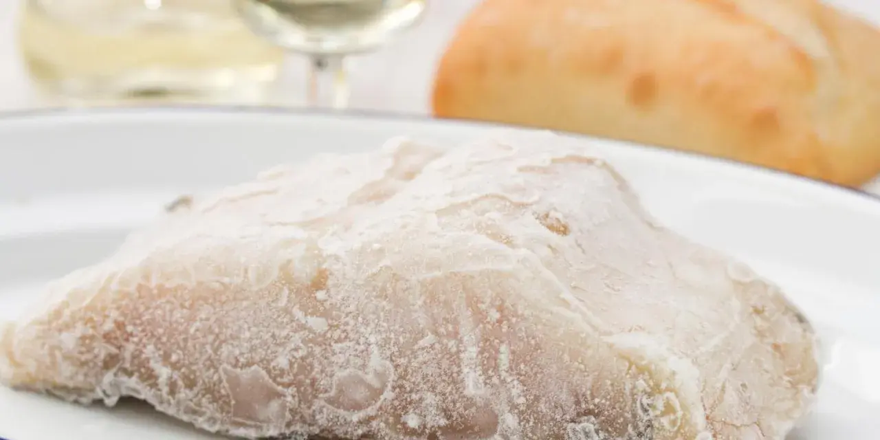 Un trozo de pescado en blanco, escarchado, listo para cocinar. Acompañado de pan y vino blanco.