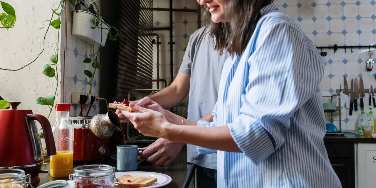 Pareja preparando el desayuno, tostadas con mermelada y café. Un momento de "bonjour" en francés para empezar el día.