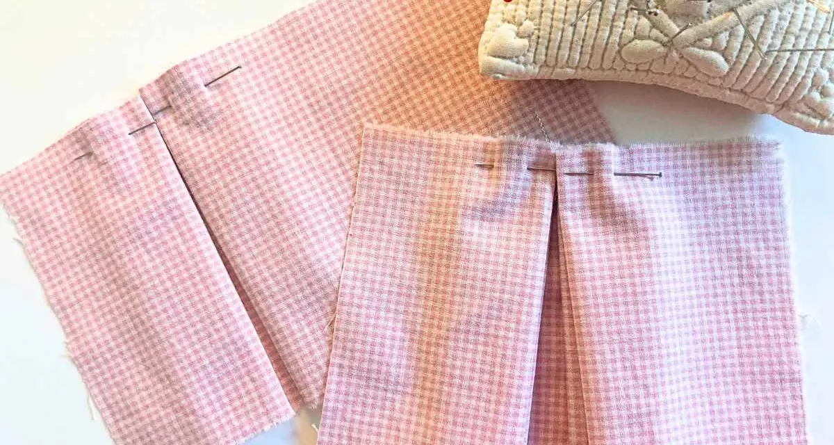 Tissu rose à carreaux avec des plis épinglés, montrant comment faire des plis en couture avec une fourchette. Coussin à épingles en arrière-plan.