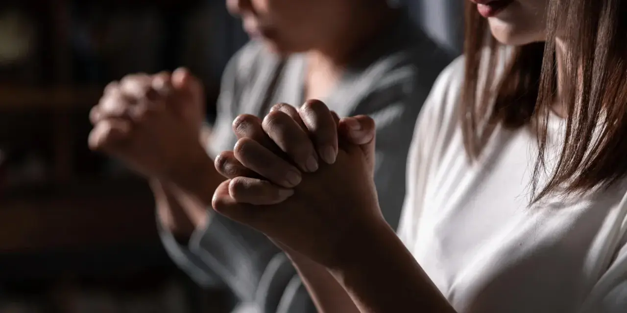 Two women pray, hands clasped. One's face is blurred, the other's lips are visible. This scene evokes the devotion of a deaconess in the bible.