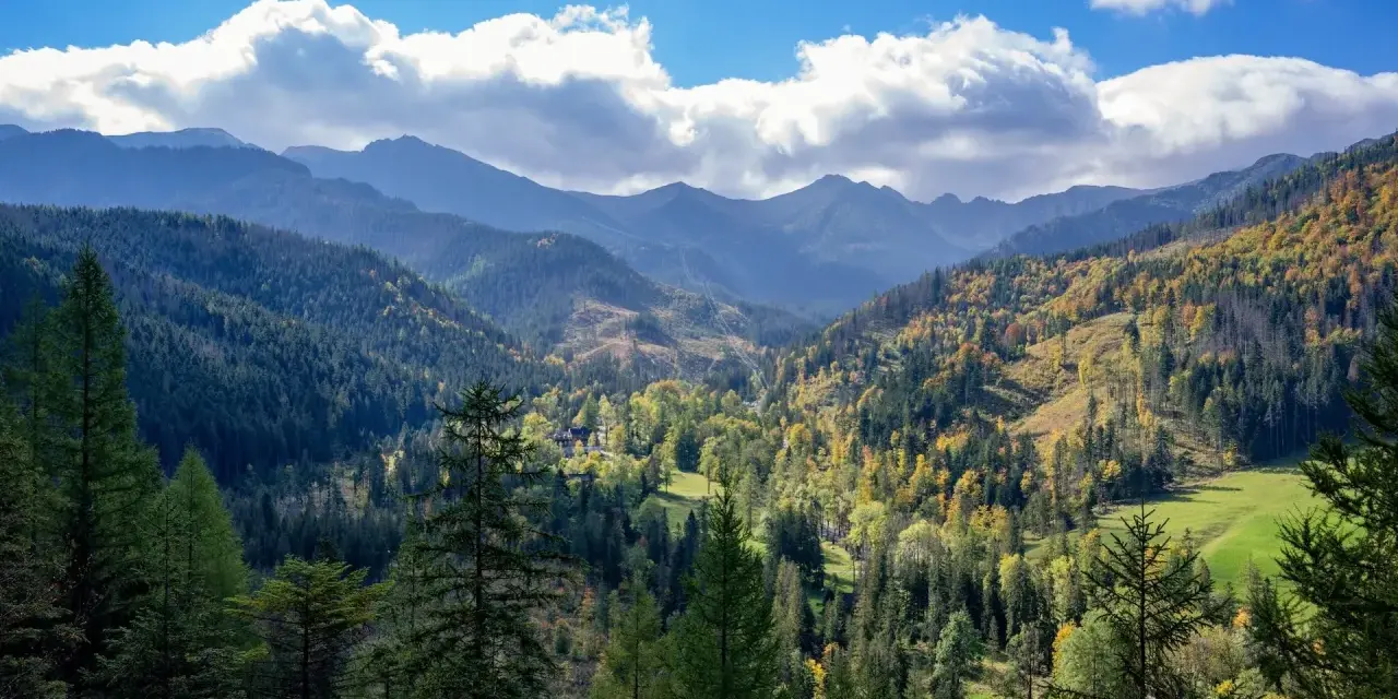 Jesienne kolory Tatr. Łatwe szczyty Tatry w jesiennej szacie, zalesione zbocza i błękitne niebo z chmurami.