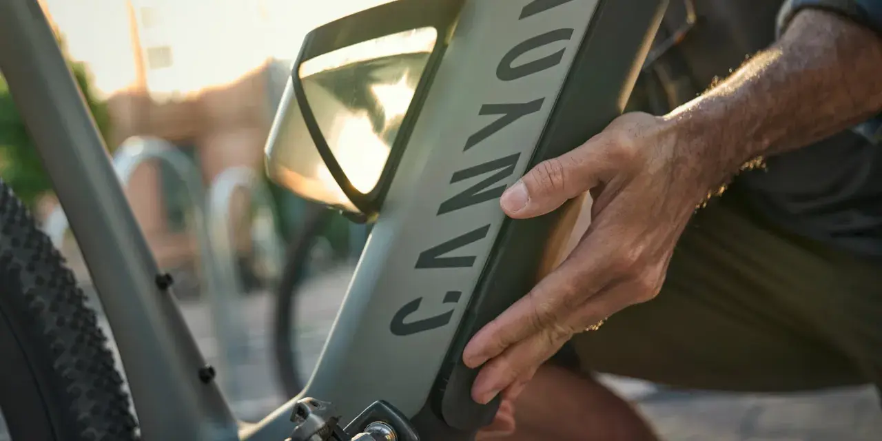 En hand justerar en elcykel. Solen skiner genom ett fönster på cykelns ram.