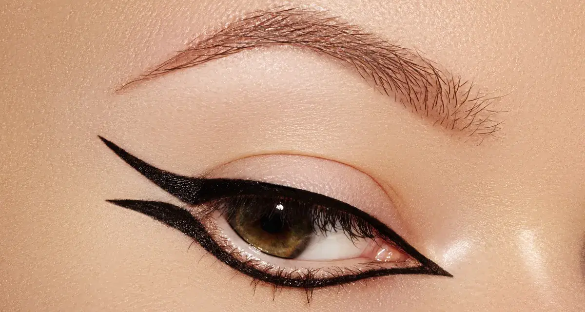 Occhio con un audace **reverse eyeliner** nero, che incornicia la palpebra inferiore e si estende verso l'alto, creando un look grafico e sofisticato.