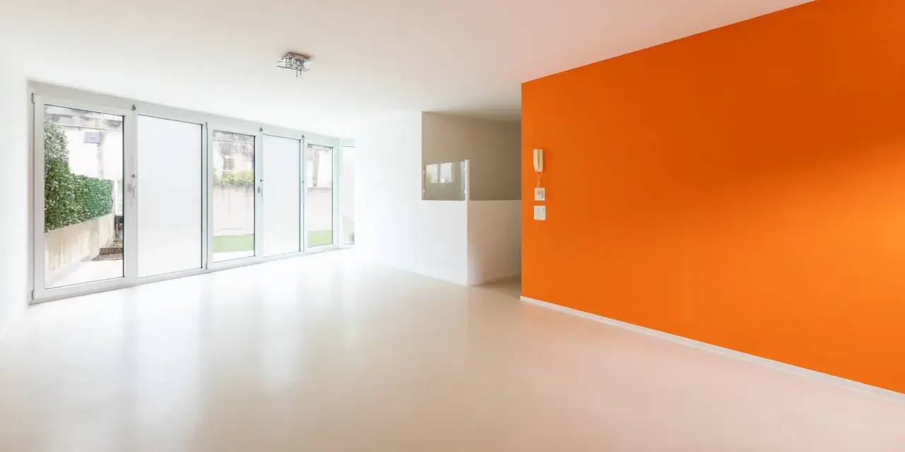 Jasne, nowoczesne wnętrze z pomarańczową ścianą i podłogą z **mikrobetonu**. Duże okna wpuszczają dużo światła.