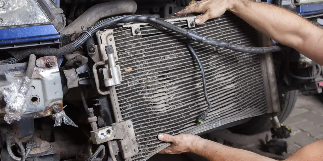 Mechanic removing a car's AC condenser, which blows hot air, for repair.